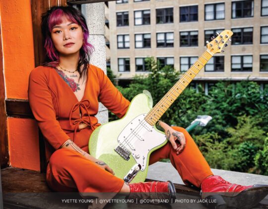 Yvette Young sitting in a window sill featured in the November 2023 Guitar Girl Magazine Calendar with an Ibanez electric guitar