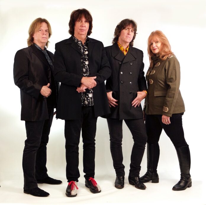 The Grip Weeds band photo featuring Dave DeSantis, Kurt Reil, Rick Reil, and Kristin Pinell Reil standing against a white background, dressed in retro-rock style.