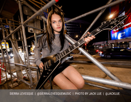 April page of the 2026 Guitar Girl Magazine calendar featuring guitarist Sierra Levesque holding an Epiphone electric guitar on a city street at night.