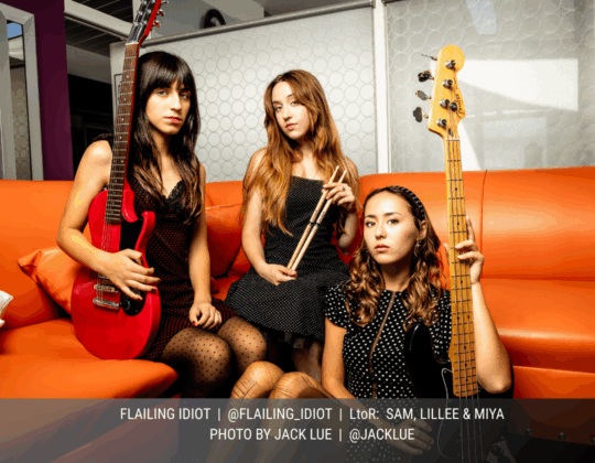 September page of the 2026 Guitar Girl Magazine calendar featuring Flailing Idiot, a female-led band seated on an orange couch holding guitar, bass, and drumsticks.