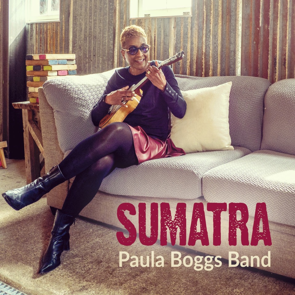 Cover art for Paula Boggs Band’s album Sumatra featuring Paula Boggs seated on a couch playing ukulele. Photo by Tom Reese.