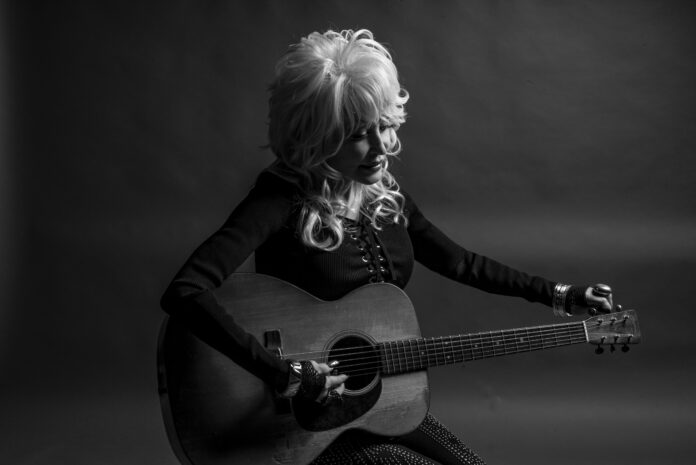 Dolly Parton seated with acoustic guitar